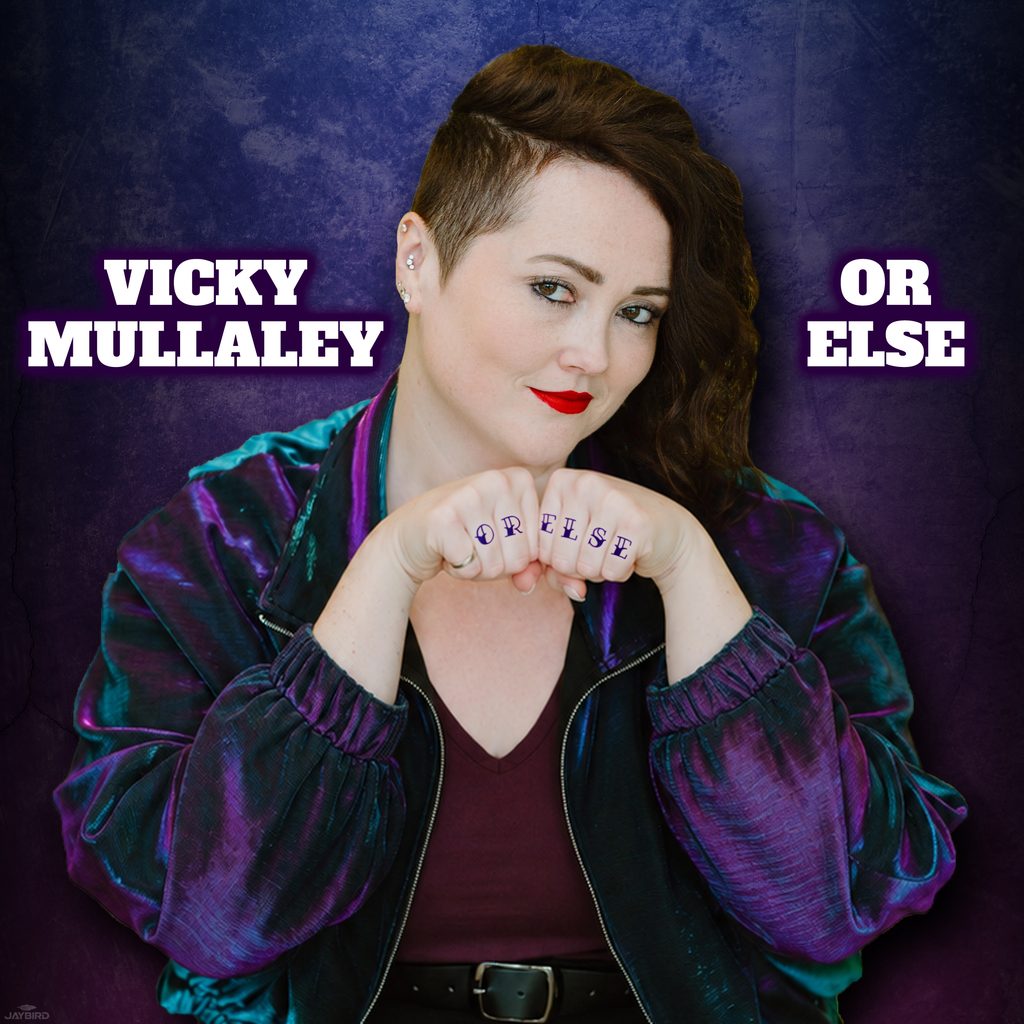 Vicky Mullaley poses with her fists raised beneath her chin, revealing “OR ELSE” tattooed across her knuckles. The bold comedy album cover features the title Or Else and Vicky’s name